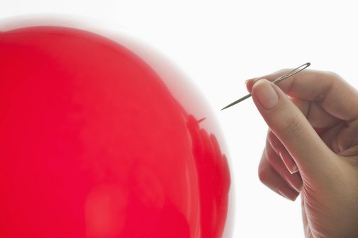 Renten-Knall Ein roter Luftballon, eine Hand, die eine Nadel hält, nähert sich.