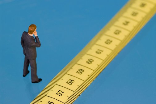 Ein Figürchen steht vor einem Maßband, auf dem die Zahlen ab 57 aufwärts zu sehen sind, als Symbol für das Renteneintrittsalter