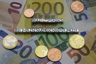 Buchstaben-Würfel bilden das Wort Beitragsbemessungsgrenze, die Buchstaben liegen auf Euro-Scheinen und Euro-Münzen