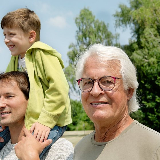 Drei Männer - ein älterer Mann schaut in die Kamera, ein jüngerer Mann blickt in die Ferne, auf seinen Schultern sitzt ein Junge.