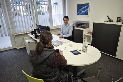 In einem B&uuml;ro einer VdK-Kreisgesch&auml;ftsstelle l&auml;sst sich ein VdK-Mitglied beraten, das mit dem R&uuml;cken zum Betrachter an einem Schreibtisch sitzt. Der Frau gegen&uuml;ber sitzt ein VdK-Sozialrechtsberater, der sie aufmerksam und freundlich anblickt. 