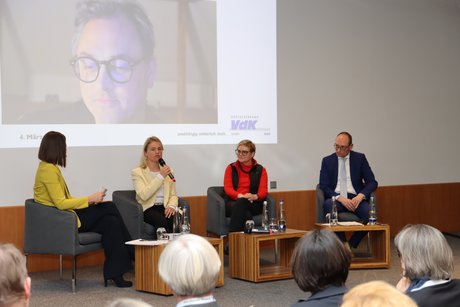 Auf dem Foto sieht man (von links): Moderatorin Isabella Kroth, VdK-Landesvorsitzende Verena Bentele, Parlamentarische Staatssekretärin im Bundesgesundheitsministerium Sabine Dittmar, Vorsitzender des Gesundheitsausschusses im Bayerischen Landtag Bernhard Seidenath und im Hintergrund auf einer Leinwand online zugeschaltet Mitglied der Regierungskommission Kliniken Prof. Dr. Christian Karagiannidis.