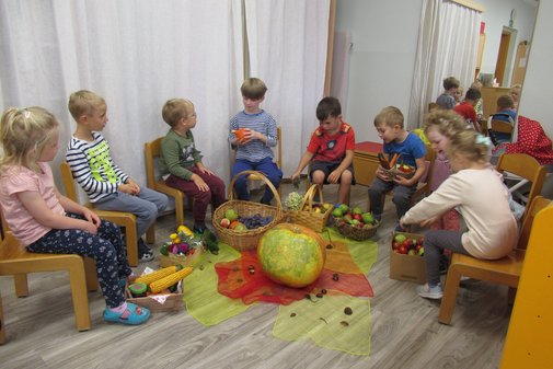 Kinder sitzen im Kreis, am Boden liegen verschiedenes Gemüse und Obst