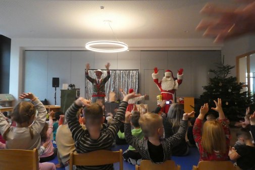 auf einer Bühne, vor der viele Kinder sitzen, wird ein Programm mit dem Weihnachtsmann vorgeführt