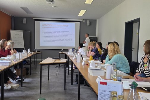 Blick in einen Seminarraum, in dem viele Personen an Tischen sitzen