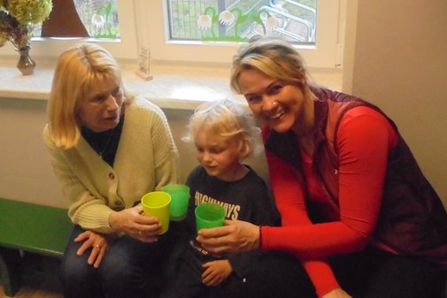 zwei Erwachsene und ein Kind prosten sich mit einem Becher zu