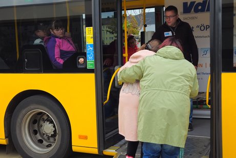 zwei Frauen steigen über eine Rampe in einen Bus ein, eine davon am Rollator