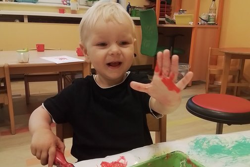 kleiner Junge malt mit Farbe, auch auf seine Hand