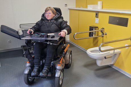 eine Frau im Rollstuhl in einem Toiletten-Container