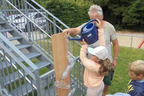ein Kind gießt mit einer Gießkanne Wasser in ein Röhrensystem