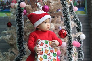 ein Baby sitzt mit einem Geschenk vor einem Weihnachtsbaum