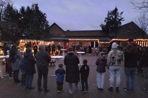 bunt beleuchtete Weihnachtsbuden, auf einem Hof, es stehen Kinder und Erwachsene davor