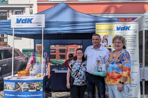 vier Personen stehen vor einem Zelt mit Infostand