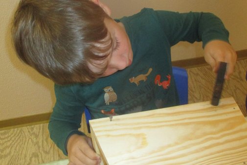 ein kleiner Junge hämmert Nägel in eine Kiste