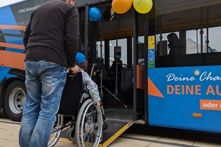 ein Mann schiebt ein Kind im Rollstuhl über eine Rampe in einen Bus