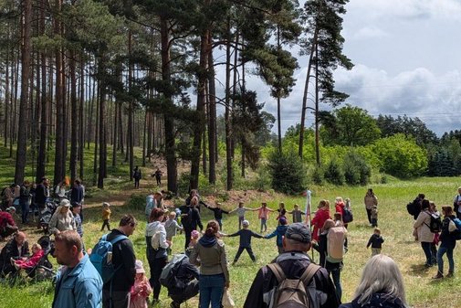 Kinder und erwachsene auf einer Wiese vor einem Wald