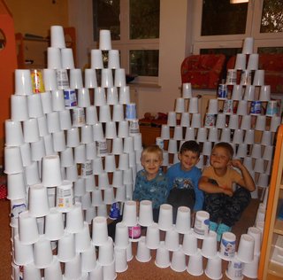 drei Kinder sitzen in einem Kreis von aufgestapelten Bechern