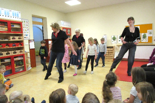 mehrere Frauen tanzen mit Kindern einen typischen Linedance, andere Kinder schauen zu