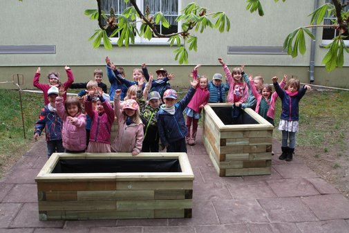 Kinder stehen um zwei Hochbeete und jubeln