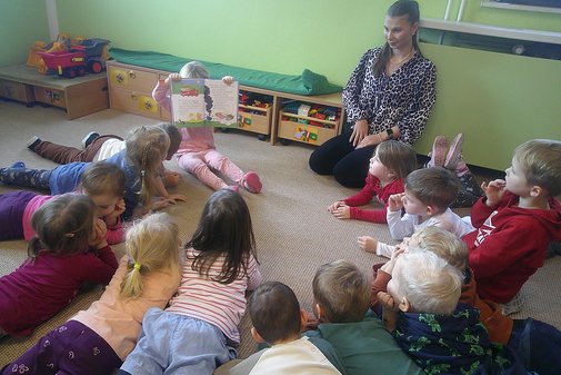 Kinder liegen im Kreis und hören einer Erzieherin zu