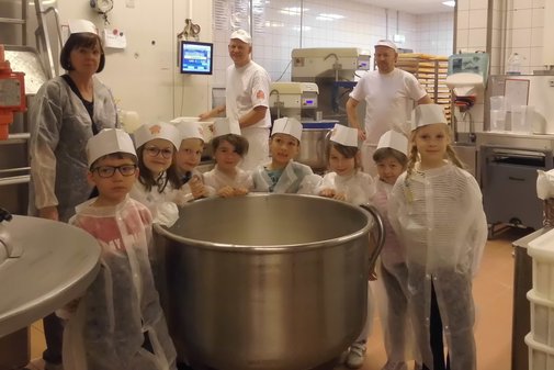 Kinder und Bäcker sowie Erzieherin stehen hinter einem großen Behälter