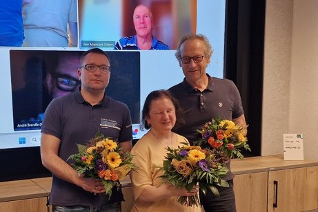 zwei Männer und eine Frau stehen nebeneinander mit Blumen