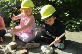 Zwei Kinder mit Bauhelm zerkleinern Steine