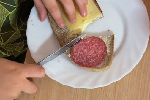 ein Kind schmiert ein Brot mit Wurst und K&auml;se
