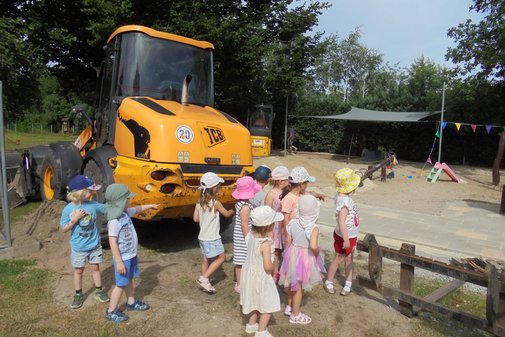Kinder stehen an einem Bagger an einer Baustelle