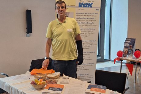 Tisch mit Werbemitteln, Vdk-Werbeaufsteller im Hintergrund, davor einem Mann