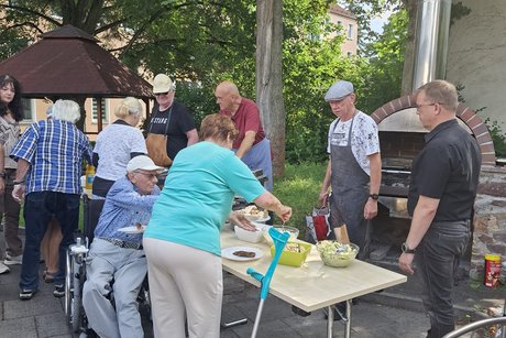 Jan Graupner und Ralph Beckert stehen hinter den Ausgabetischen mit dem Grillgut und die Mitglieder nehmen sich u.a. Salate