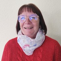 Frau mit rotem Pullover, weißem Halstuch, mittellange dunkle Harre mit Brille, freundlich lächelnd