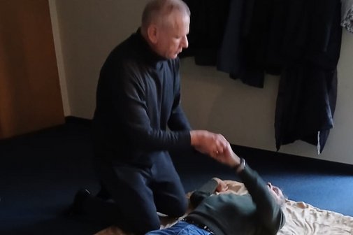 Ein Mann liegt auf dem Boden. Ein zweiter kniet neben ihm, h&auml;lt seine Hand und spricht ihm gut zu.