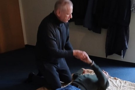 Ein Mann liegt auf dem Boden. Ein zweiter kniet neben ihm, h&auml;lt seine Hand und spricht ihm gut zu.