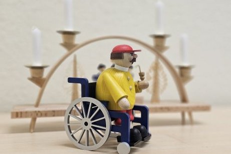 R&auml;uchermann im Rollstuhl steht vor einem Schwibbogen