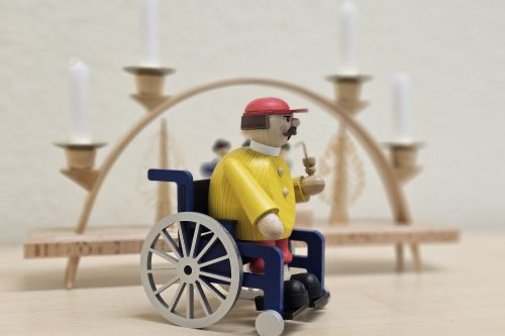 R&auml;uchermann im Rollstuhl steht vor einem Schwibbogen
