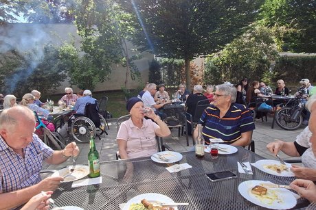 Männer und Frauen sitzen an mehreren Tischen und essen Roster und Steacks im Freien