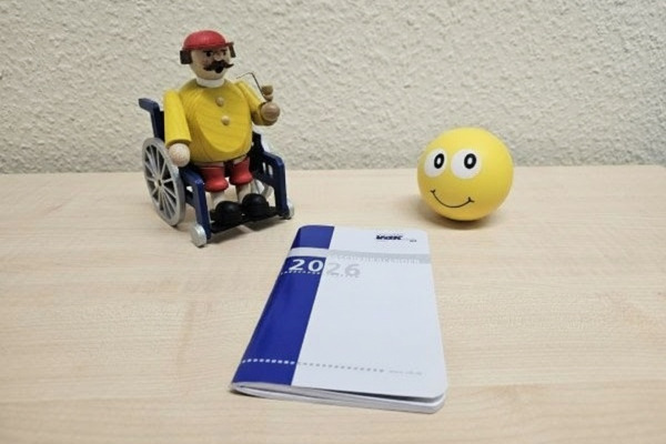 Ein Kalender 2026 liegt vor einem im Rollstuhl sitzenden R&auml;uchermann