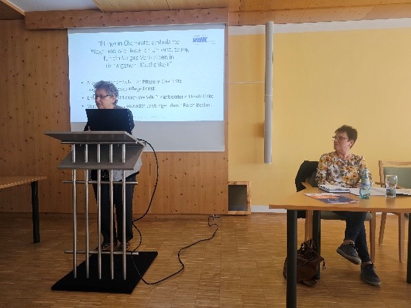 Frau Liske steht links hinter einem Pult und Frau Lorenz sitzt rechts an einem Tisch